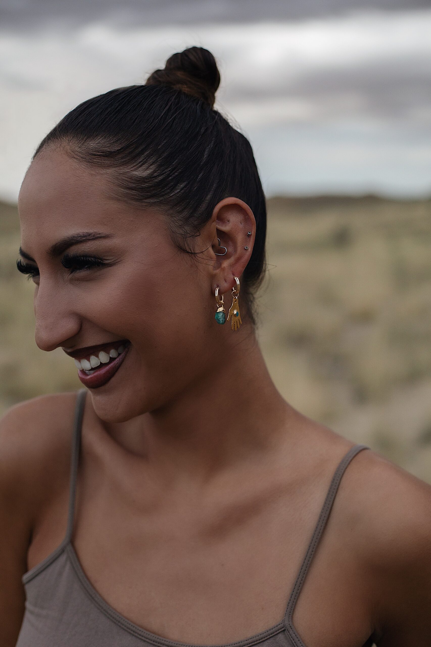 Close-up of a smiling woman wearing multiple gold and turquoise earrings with a sleek top bun, set against a desert background, used to increase brand awareness through authentic and expressive branding photography.